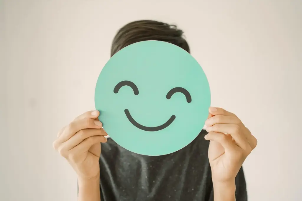 Happy mixed Asian teen boy holding smile emoji face, positive mental health concept